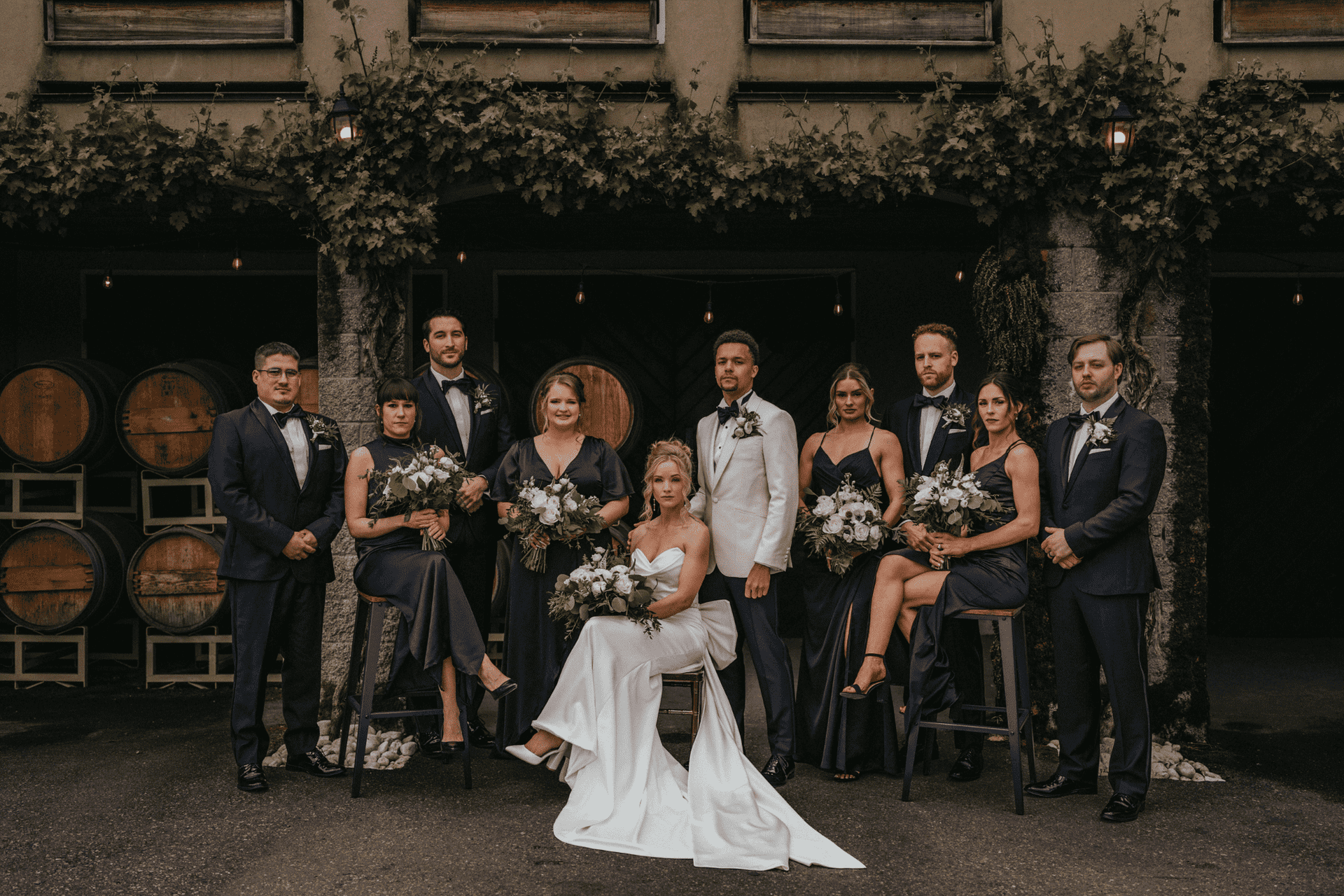 Bridal party posing with bridesmaids and groomsmen in an elegant outdoor setting, holding flowers.